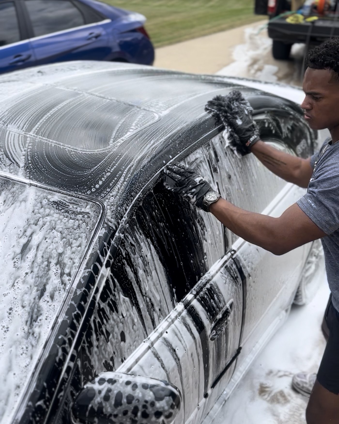 A detailer hand-washing a foam-covered sedan outdoors